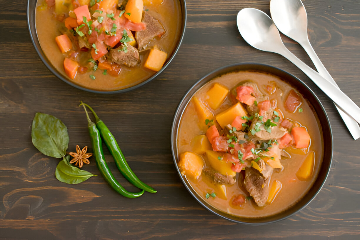 Two bowls of hearty meat and vegetable stew with spices on a wooden table.