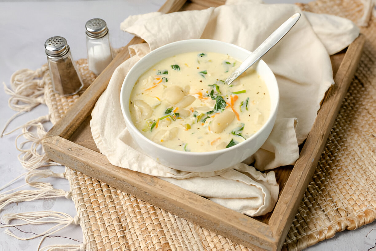 A bowl of creamy soup with vegetables and gnocchi served on a wooden tray with salt and pepper shakers