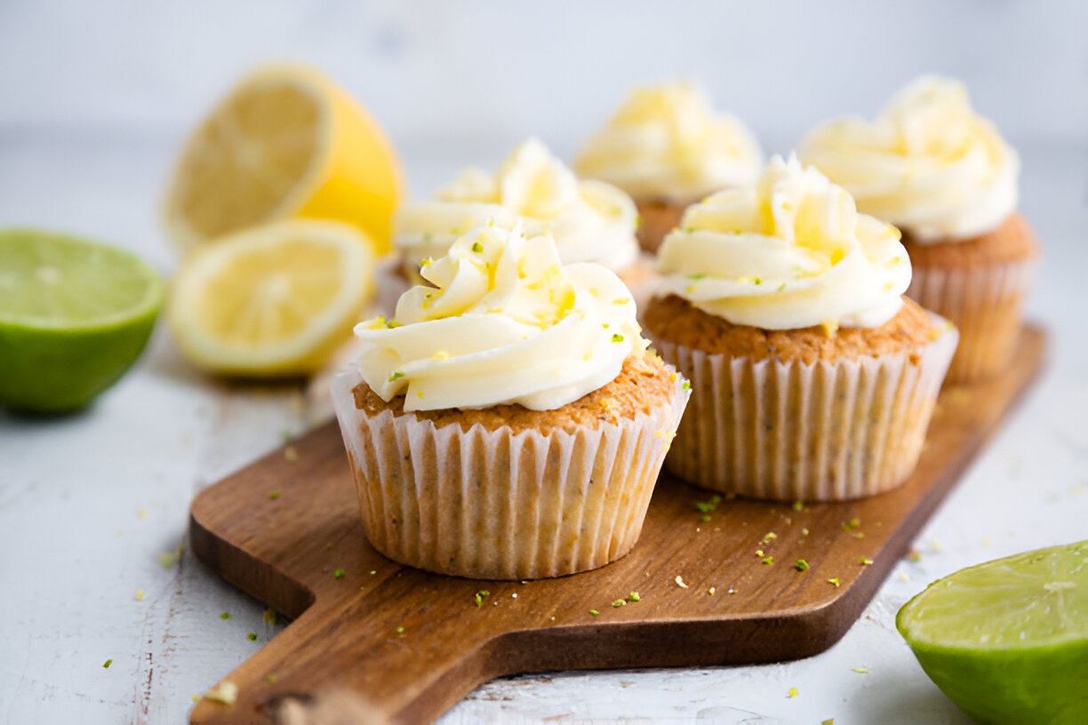 Delicious lemon-lime cupcakes with creamy frosting on a wooden board, surrounded by lime and lemon halves.