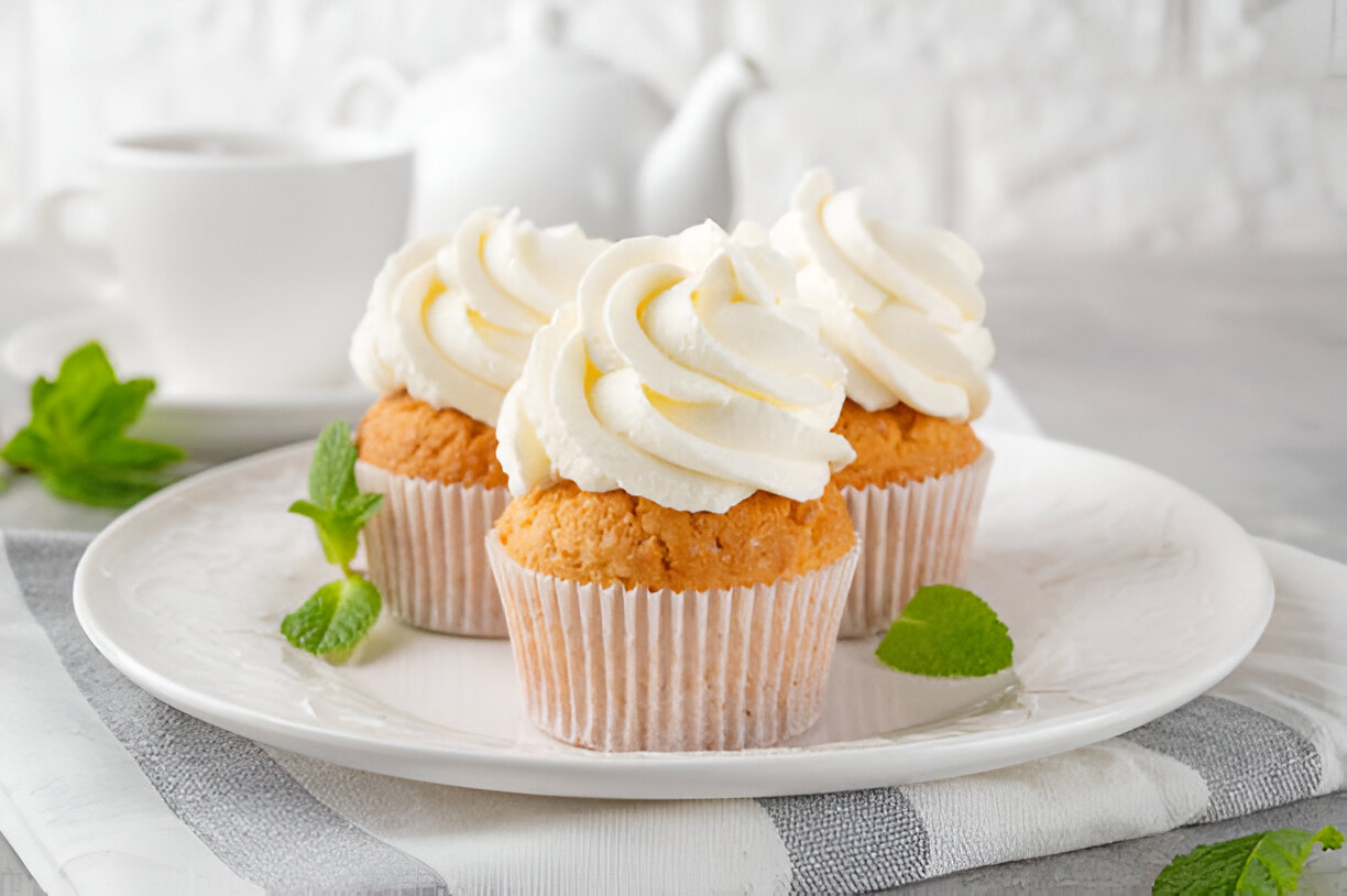 Three vanilla cupcakes with white frosting on a plate garnished with mint leaves.
