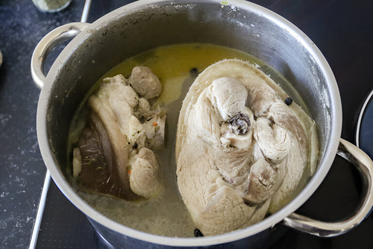 A pot of boiling meat in a broth on the stove, showcasing large cuts of meat in the water.