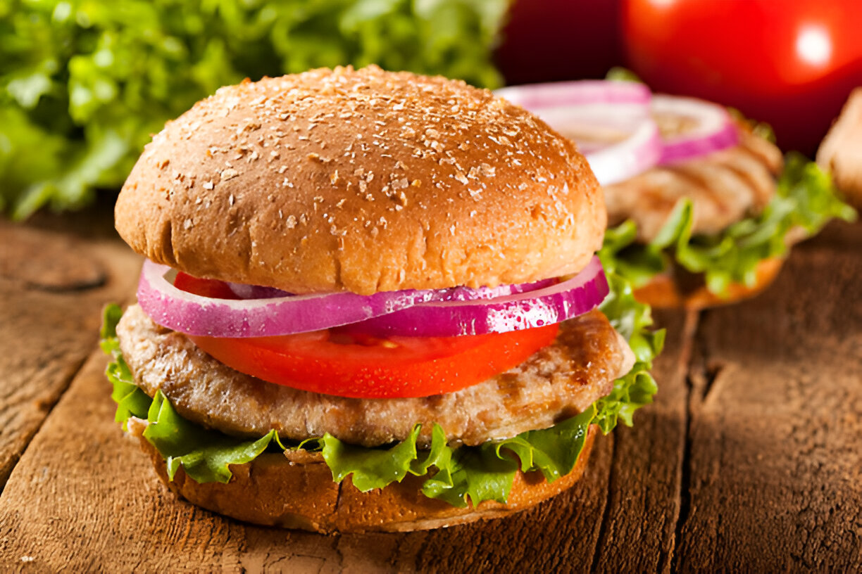 A close-up of a delicious burger made with a sesame seed bun, lettuce, tomato, red onion, and a patty, set on a wooden surface.