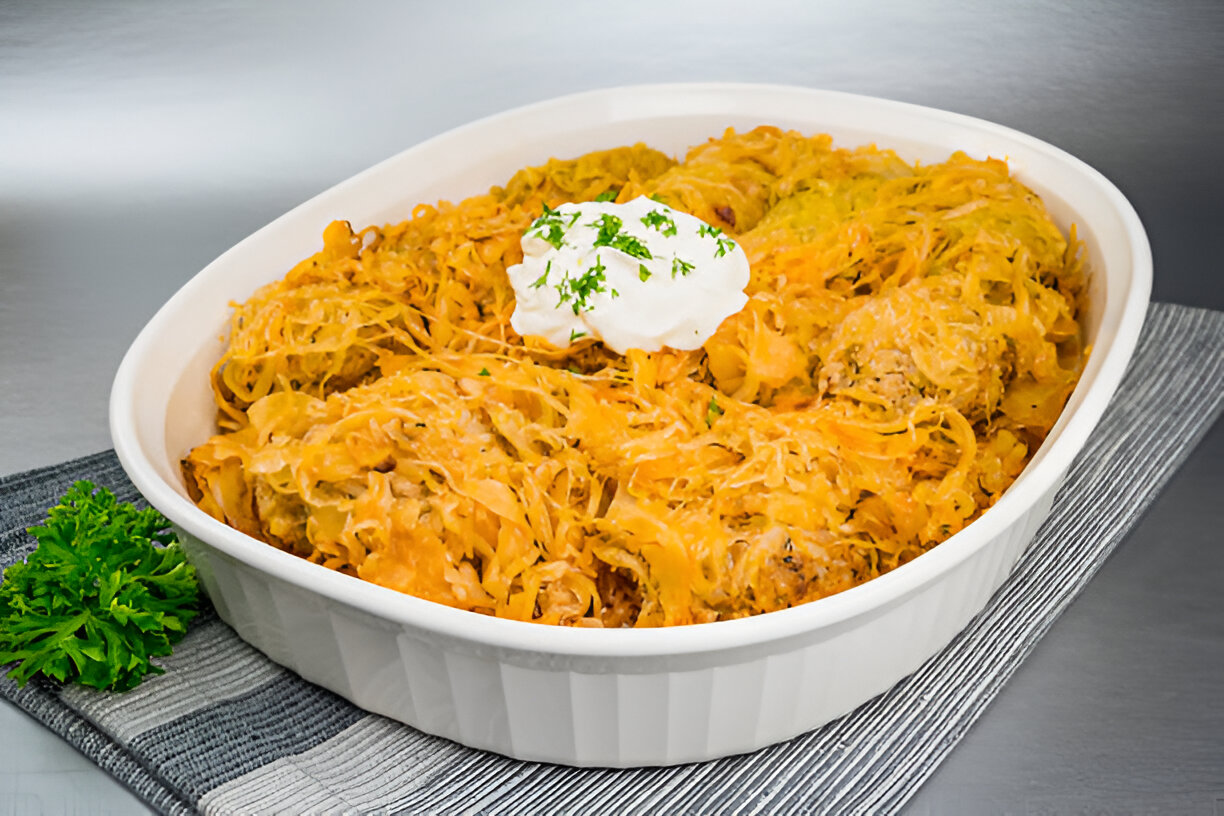 A casserole dish filled with a cheesy noodle dish topped with sour cream and green garnish