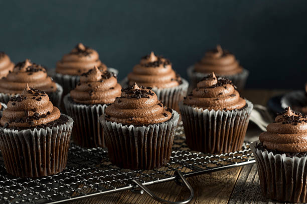 A close-up view of chocolate cupcakes with swirls of frosting topped with chocolate sprinkles on a wire rack.