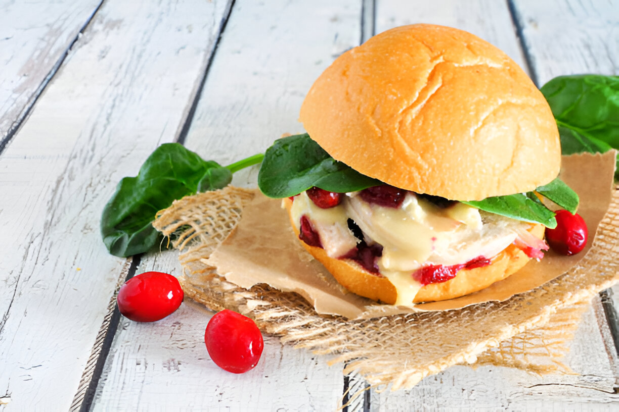A delicious sandwich featuring a soft bun filled with creamy sauce, spinach, and garnished with red berries on a rustic wooden backdrop.