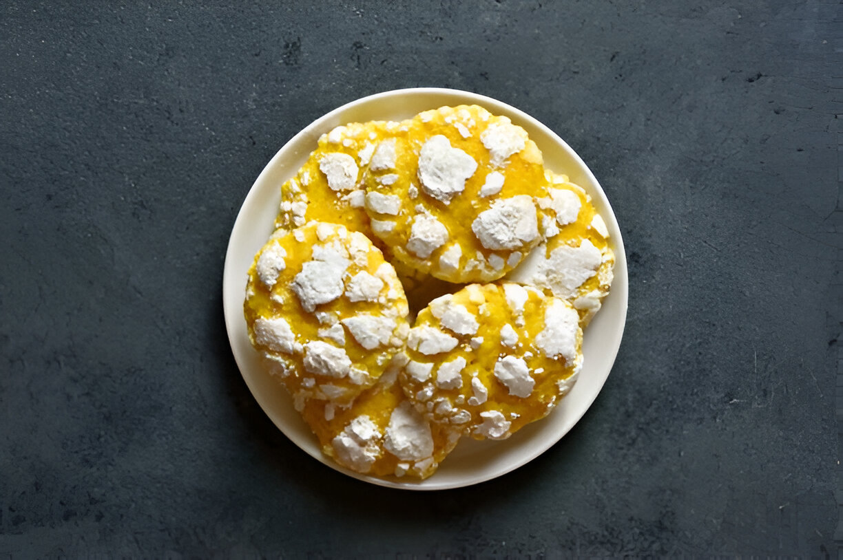 A plate of lemon crinkle cookies topped with powdered sugar on a dark background