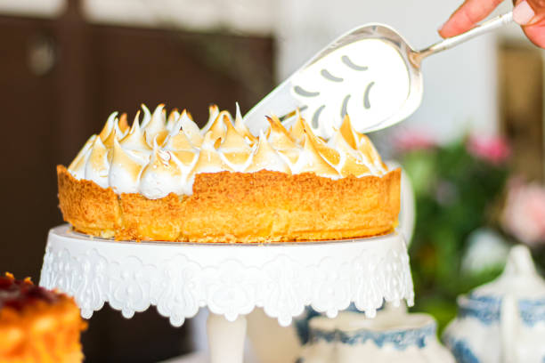 A person serving a beautiful meringue-topped cake from a white cake stand.