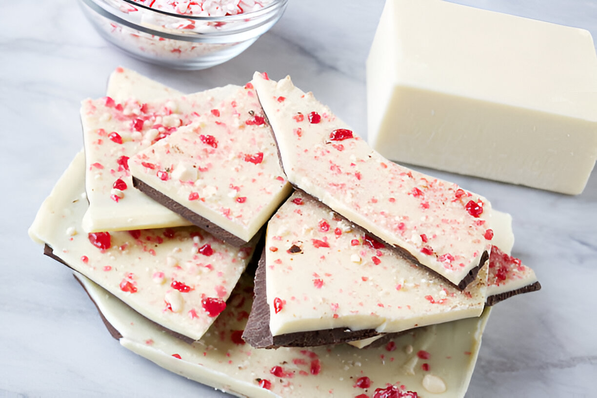 Pieces of peppermint bark on a plate with a bowl of crushed peppermint and a block of white chocolate in the background.