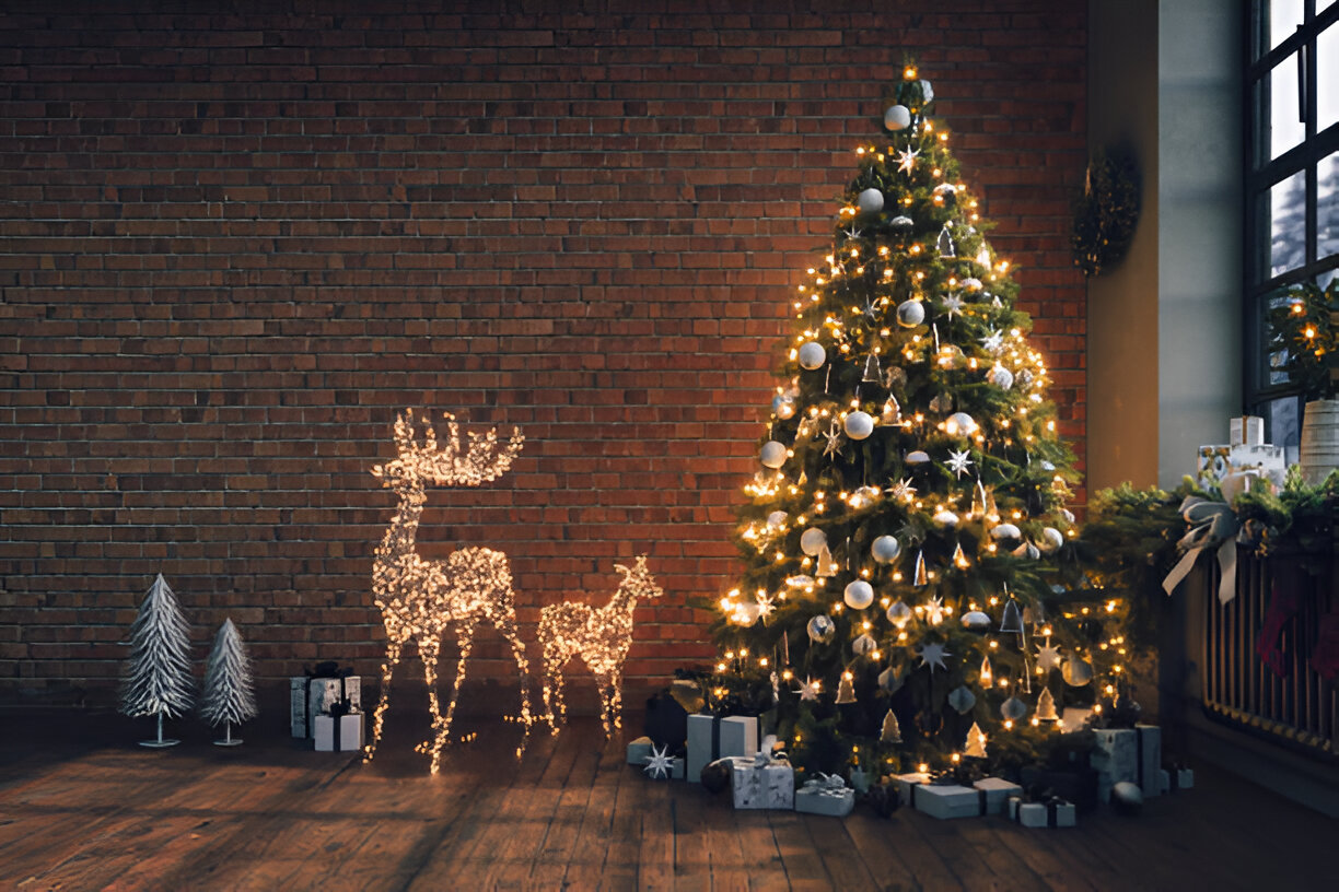 A beautifully decorated Christmas tree with lights and ornaments next to a lighted reindeer decoration in a cozy room with brick walls.