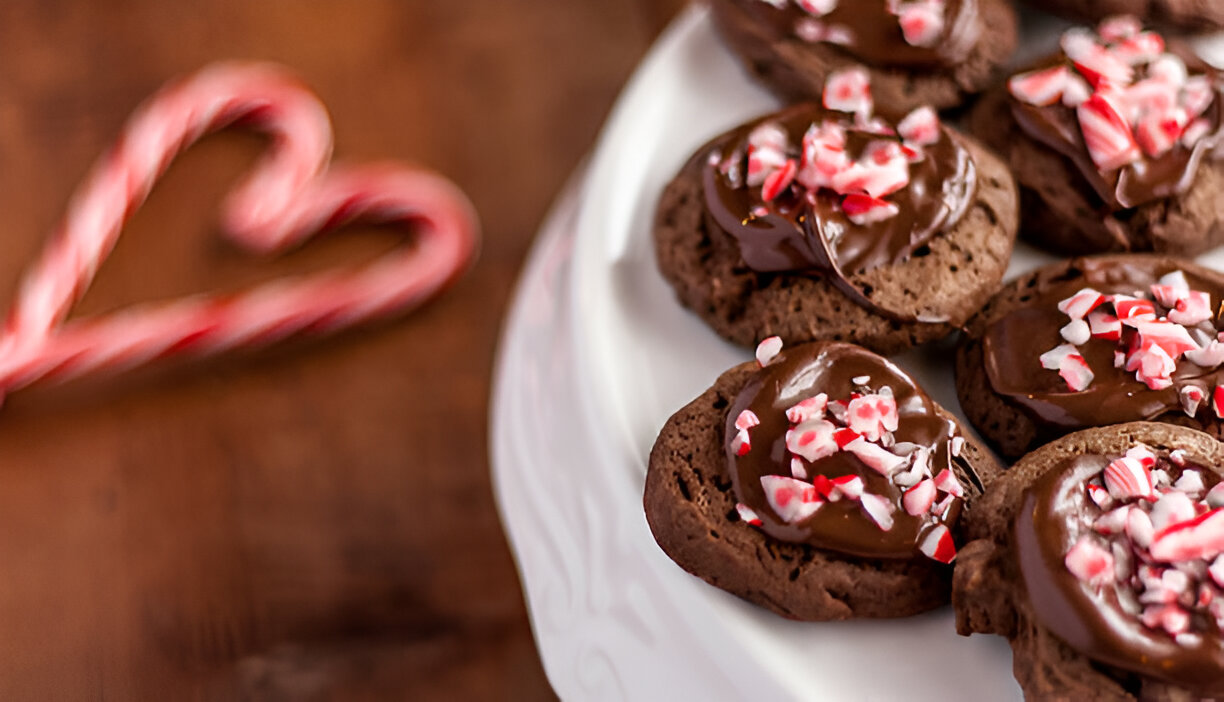 Delicious chocolate cookies topped with crushed peppermint, placed on a white plate with a candy cane heart in the background.