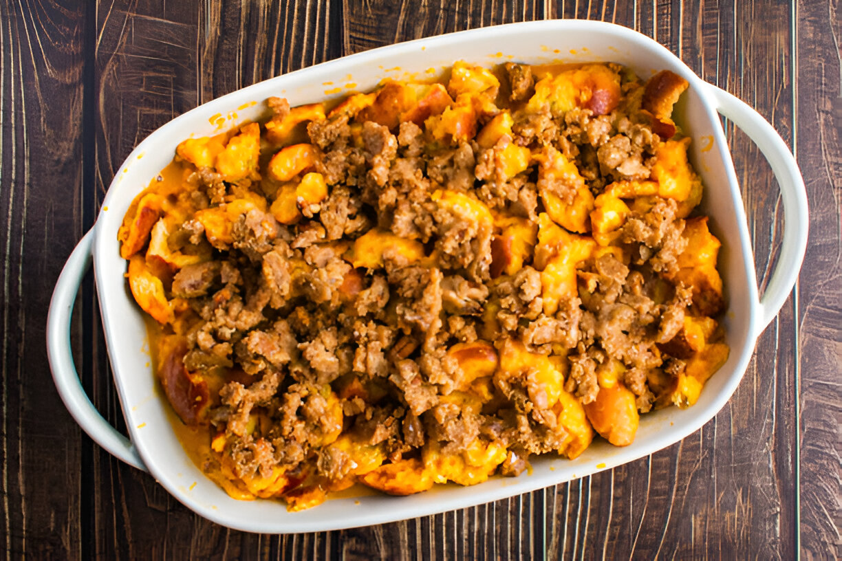 Baked casserole dish filled with cheesy pasta and seasoned meat topping on a wooden table.