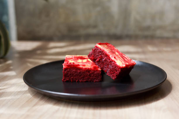 Two pieces of red velvet dessert on a black plate, placed on a wooden surface.