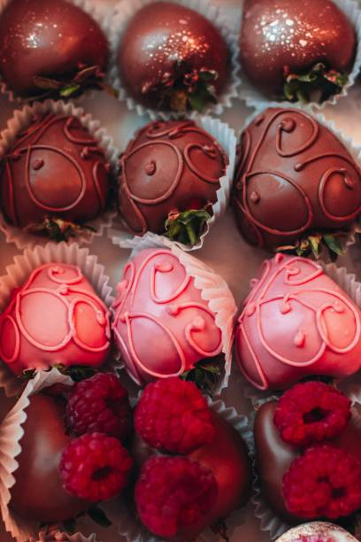 An assortment of chocolate-covered strawberries, including pink and dark chocolate varieties, displayed in a decorative box.