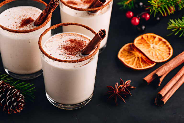 Creamy holiday drinks garnished with cinnamon sticks and spices on a dark surface