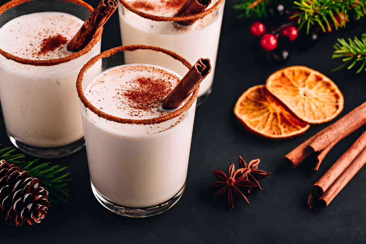Creamy holiday drinks garnished with cinnamon sticks and spices on a dark surface