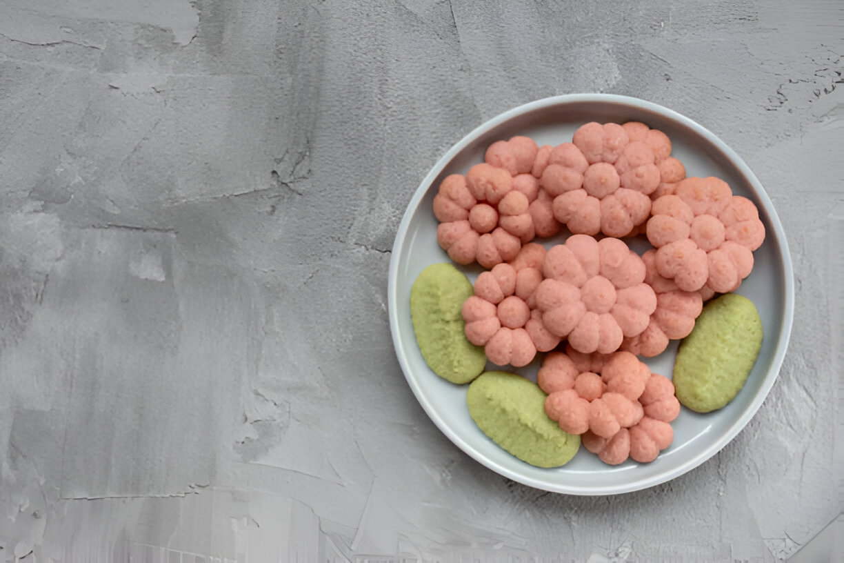A plate of colorful snacks shaped like flowers and vegetables, featuring pink floral snacks alongside green oval-shaped snacks.
