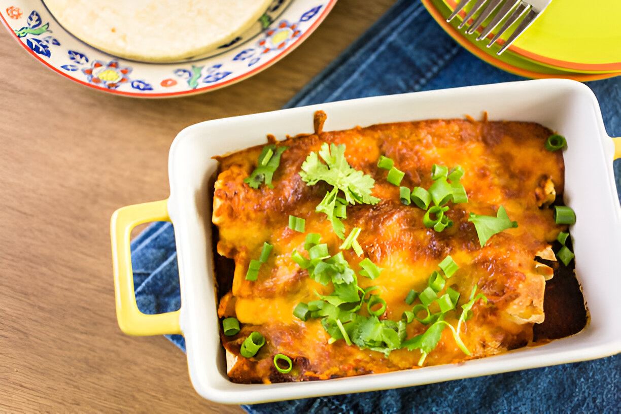 A delicious dish of enchiladas topped with cilantro and green onions served in a white baking dish.