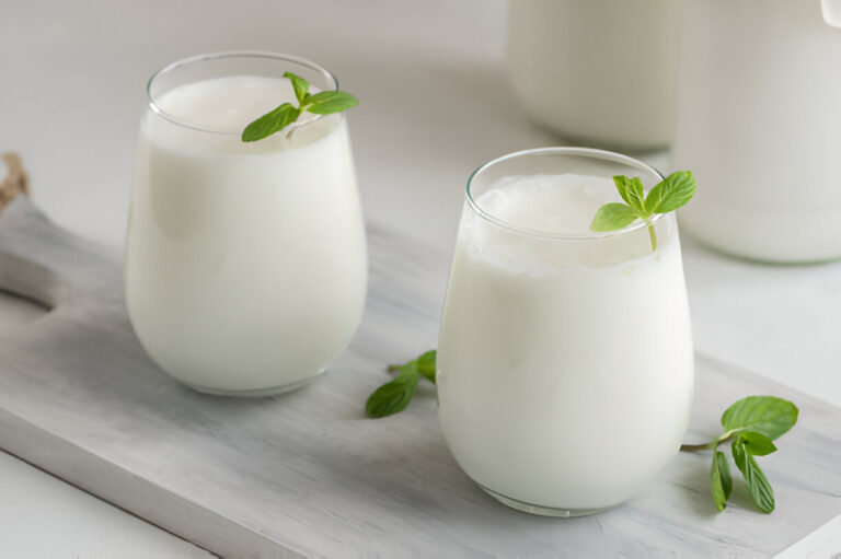 Two glasses of creamy white drink garnished with fresh mint leaves on a wooden tray