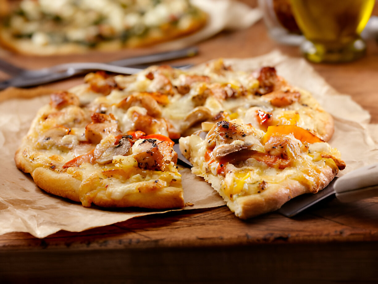 A delicious pizza topped with chicken, cheese, and colorful vegetables on a wooden surface.