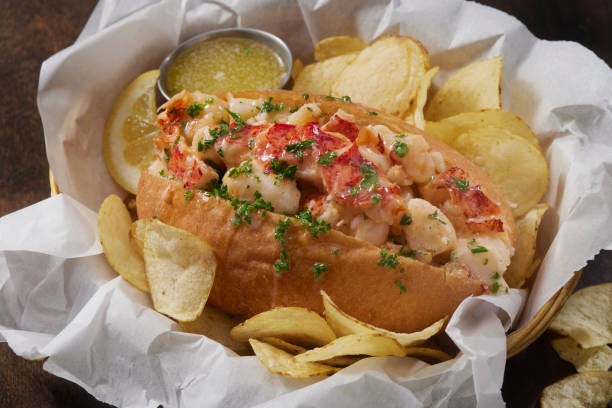A delicious lobster roll served with potato chips and a side of lemon and butter sauce.