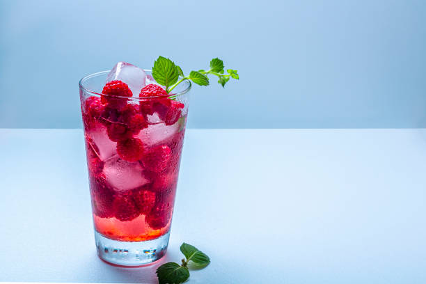 A refreshing glass of raspberry drink with ice and mint garnish on a light background.