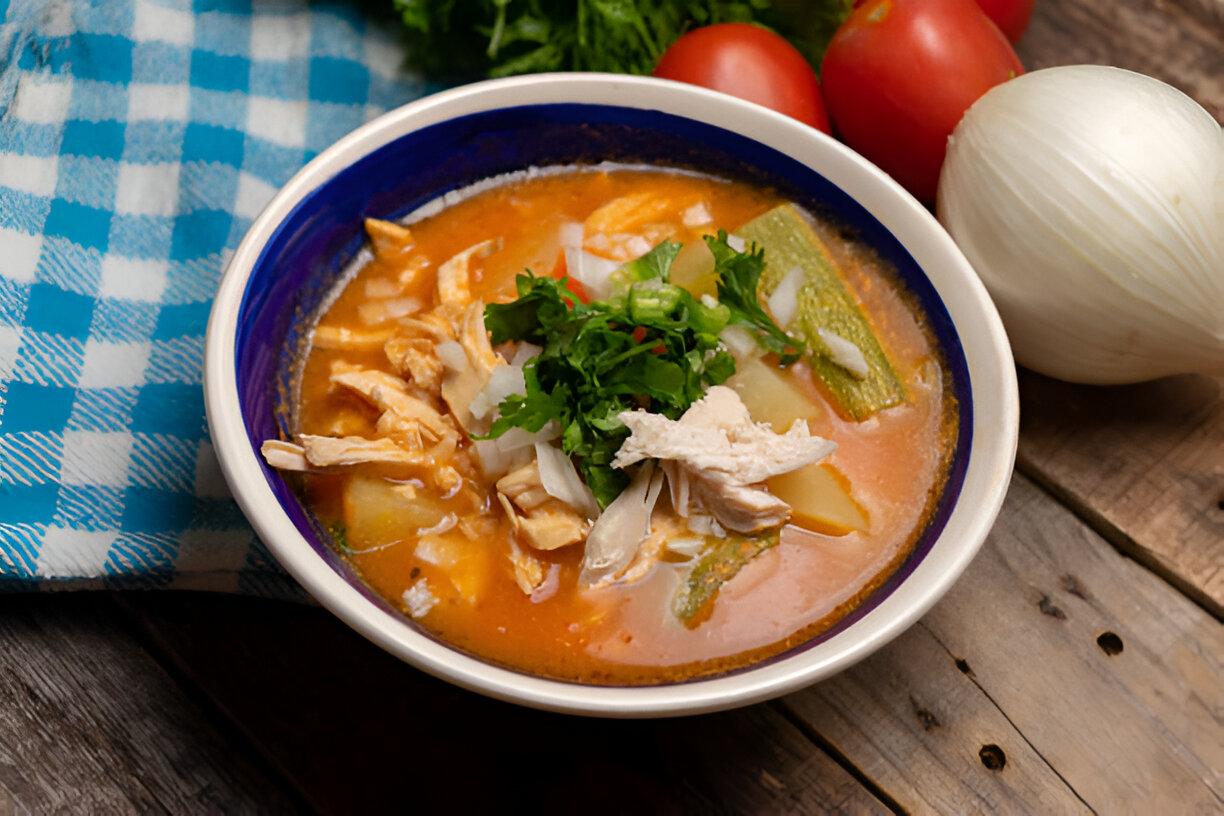 Bowl of flavorful chicken soup garnished with cilantro, surrounded by vegetables
