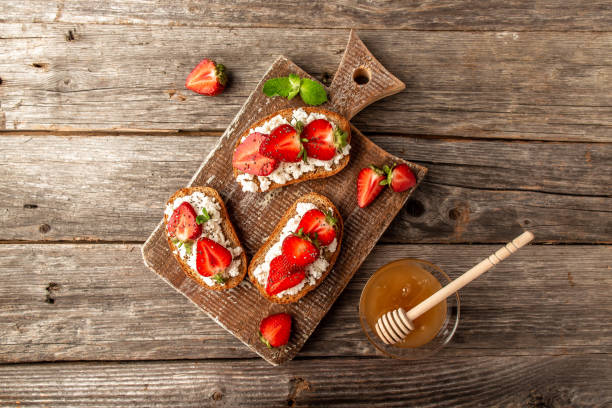 Sliced bread topped with fresh strawberries and cream cheese on a wooden cutting board