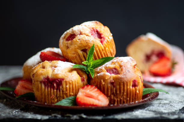 A plate of freshly baked strawberry muffins garnished with mint leaves and fresh strawberries.