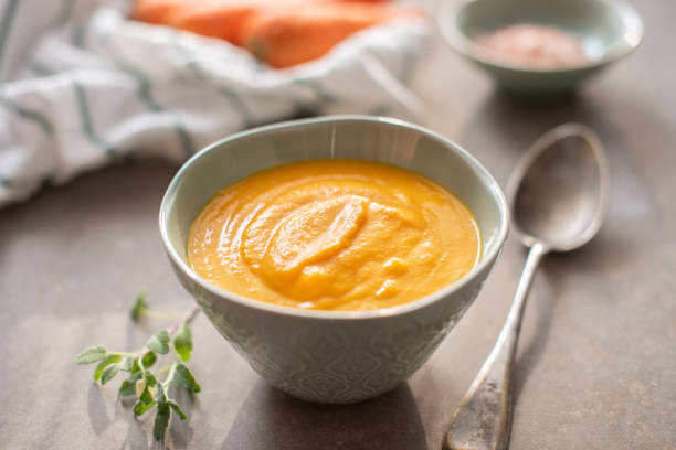 A bowl of smooth, creamy orange soup with a spoon beside it, garnished with fresh herbs.