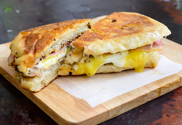 A delicious sandwich cut in half, showcasing layers of cheese, ham, and an egg, served on a wooden cutting board.