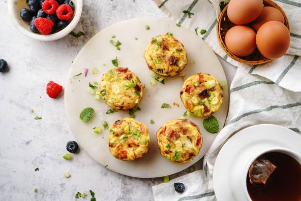 A plate of baked egg muffins with herbs and vegetables, accompanied by fresh berries and a cup of tea.