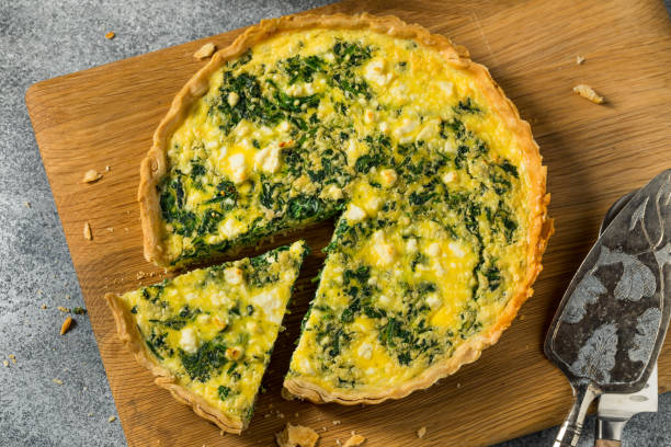 A freshly baked spinach and cheese quiche on a round wooden cutting board with a slice removed.