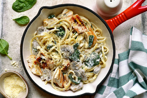 A creamy pasta dish with grilled chicken, spinach, and mushrooms in a skillet
