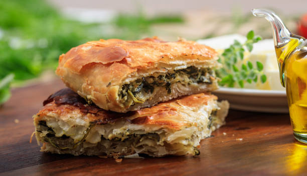 Two layers of flaky, golden-brown pastry with green filling, served with olive oil and fresh herbs.