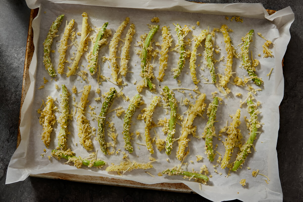 A baking tray lined with parchment paper holding unbaked, breaded green vegetables.