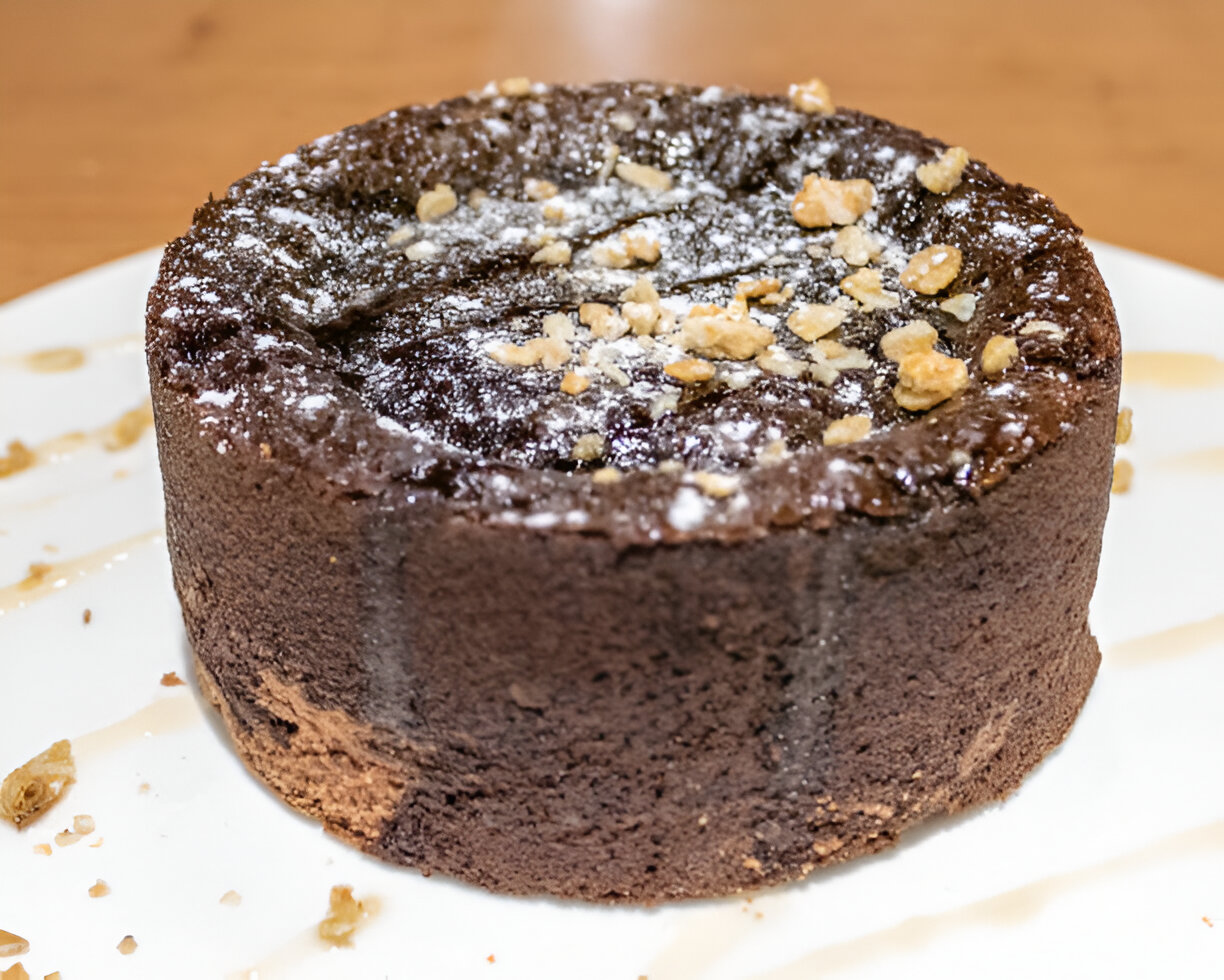 A delicious chocolate cake topped with powdered sugar and crushed nuts on a white plate.