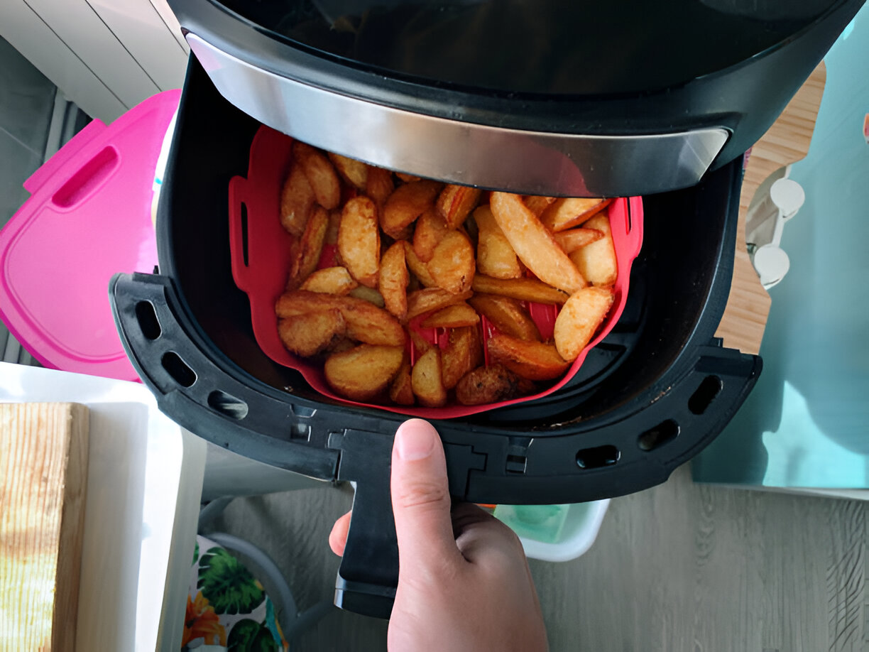 A hand holding an air fryer basket filled with golden-brown potato wedges.