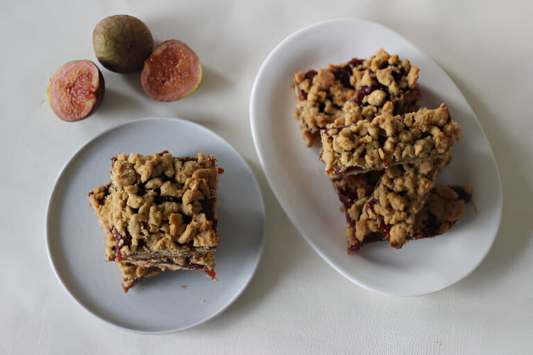 A plate of freshly baked fig crumble bars served with sliced figs on a white table.