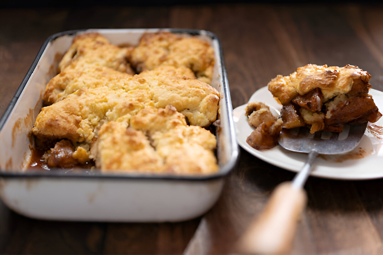 A freshly baked cobbler in a rectangular dish with a serving on a plate, showcasing a golden-brown crust.
