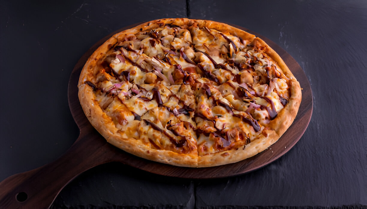 A freshly baked pizza with barbecue chicken, cheese, and drizzled sauce on a wooden serving board