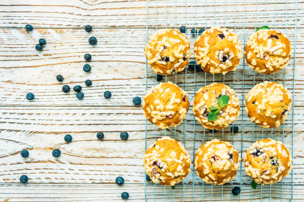 Freshly baked muffins topped with crumbly texture on a wire rack, with scattered blueberries around them.