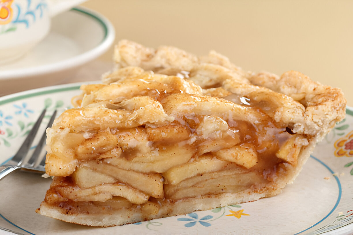 A slice of apple pie on a decorative plate with a fork beside it.