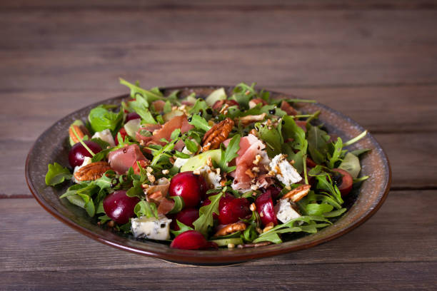 A colorful salad with arugula, grapes, prosciutto, nuts, and blue cheese in a decorative bowl.
