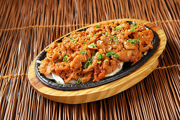 Sizzling plate of seasoned meat served on a wooden platter with sesame seeds and chopped green onions.