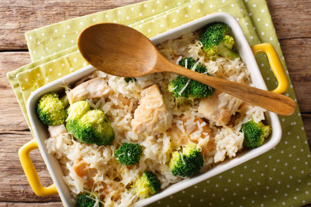 A delicious dish of chicken, broccoli, and rice in a white casserole dish with a wooden spoon on a polka-dotted napkin.