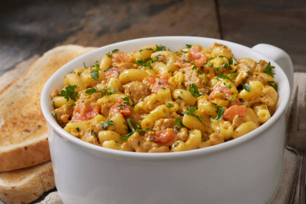 A bowl of creamy pasta with chicken, tomatoes, and herbs, accompanied by slices of toasted bread.