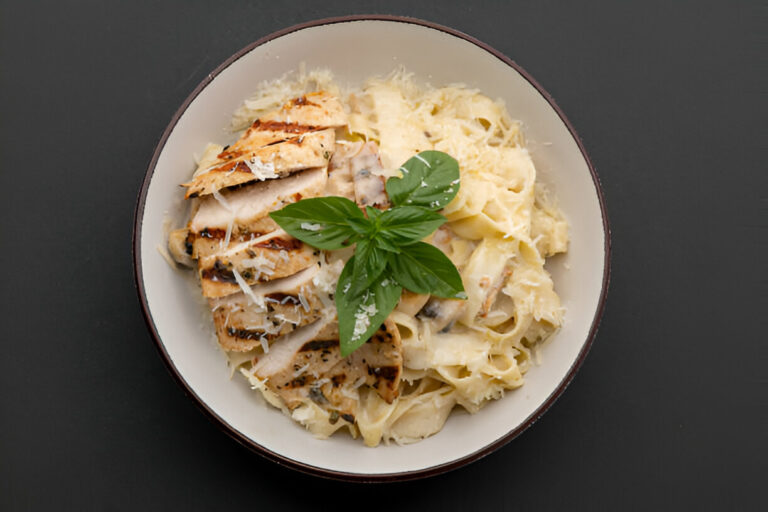 A bowl of fettuccine pasta topped with grilled chicken, creamy sauce, and fresh basil leaves.