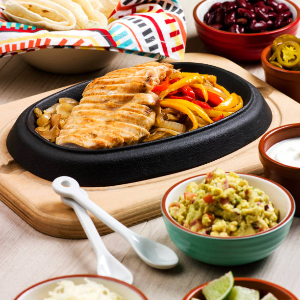 Sizzling chicken fajitas with colorful bell peppers served on a hot stone plate, surrounded by various toppings.