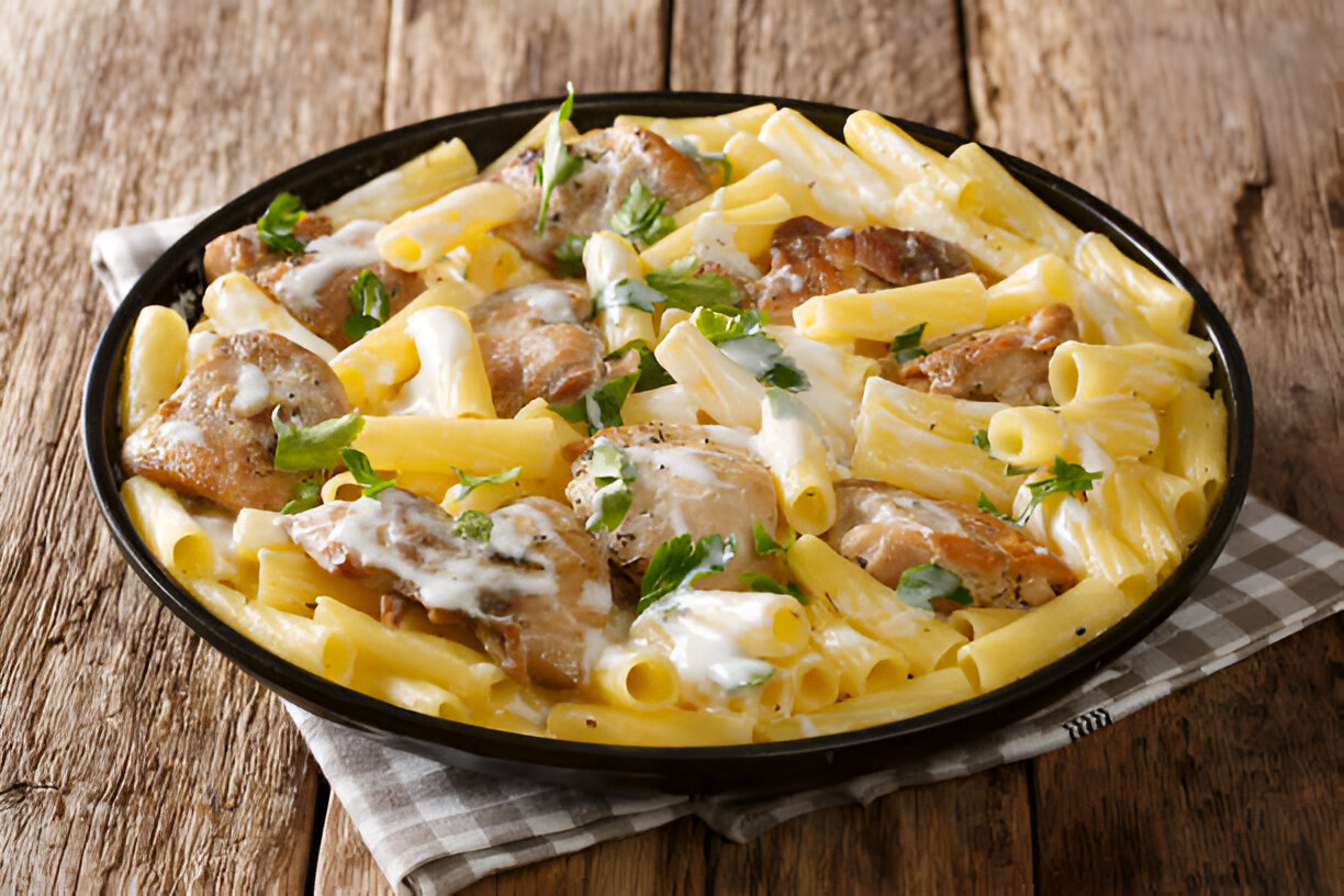 A creamy pasta dish with chicken and herbs served in a black bowl on a wooden table.