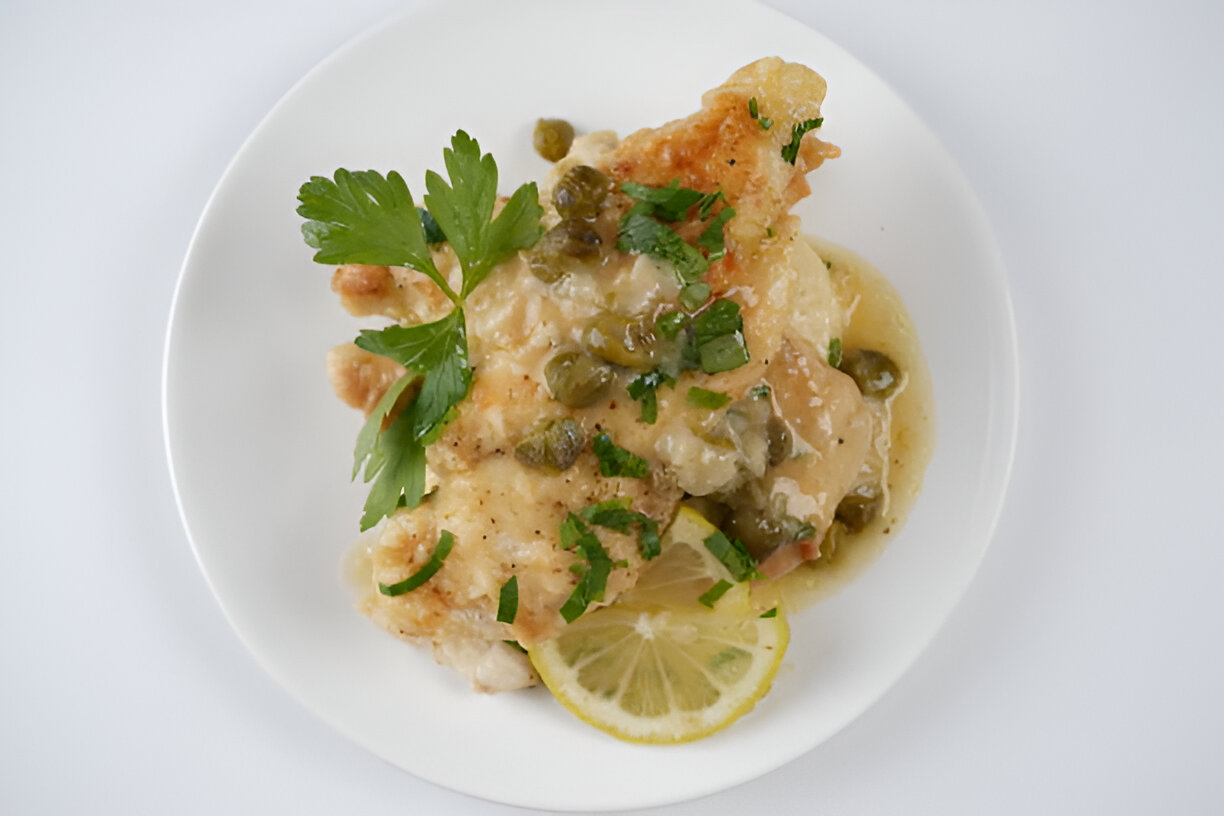 A plate of fish topped with capers, herbs, and lemon slices.